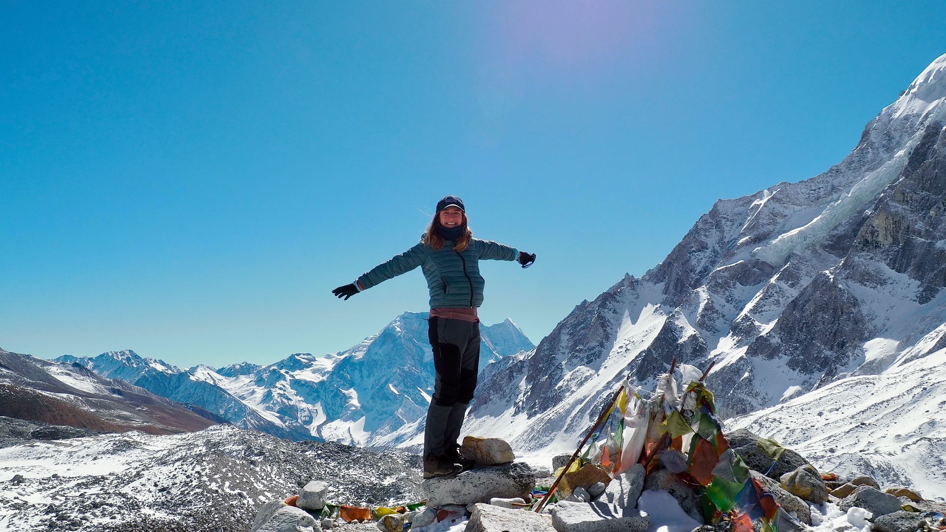 A trekker celebrates beside prayer flags at the summit.